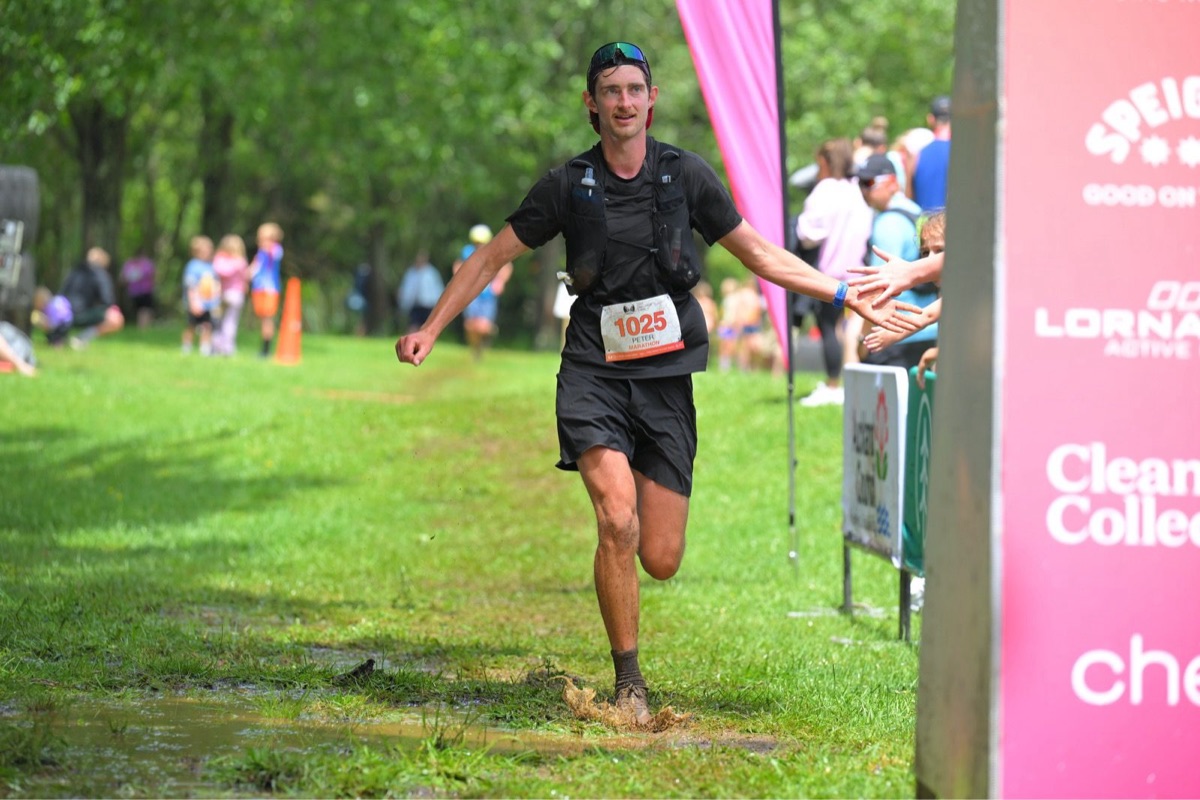 Pete running through the finish of a muddy marathon